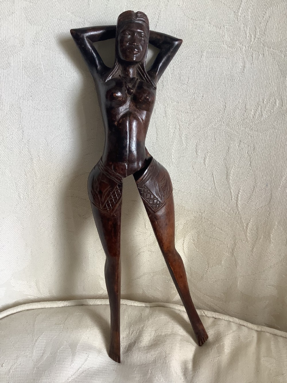 A hand-carved dark wood nutcracker sculpted in the form of a standing woman with her arms raised behind her head. View V