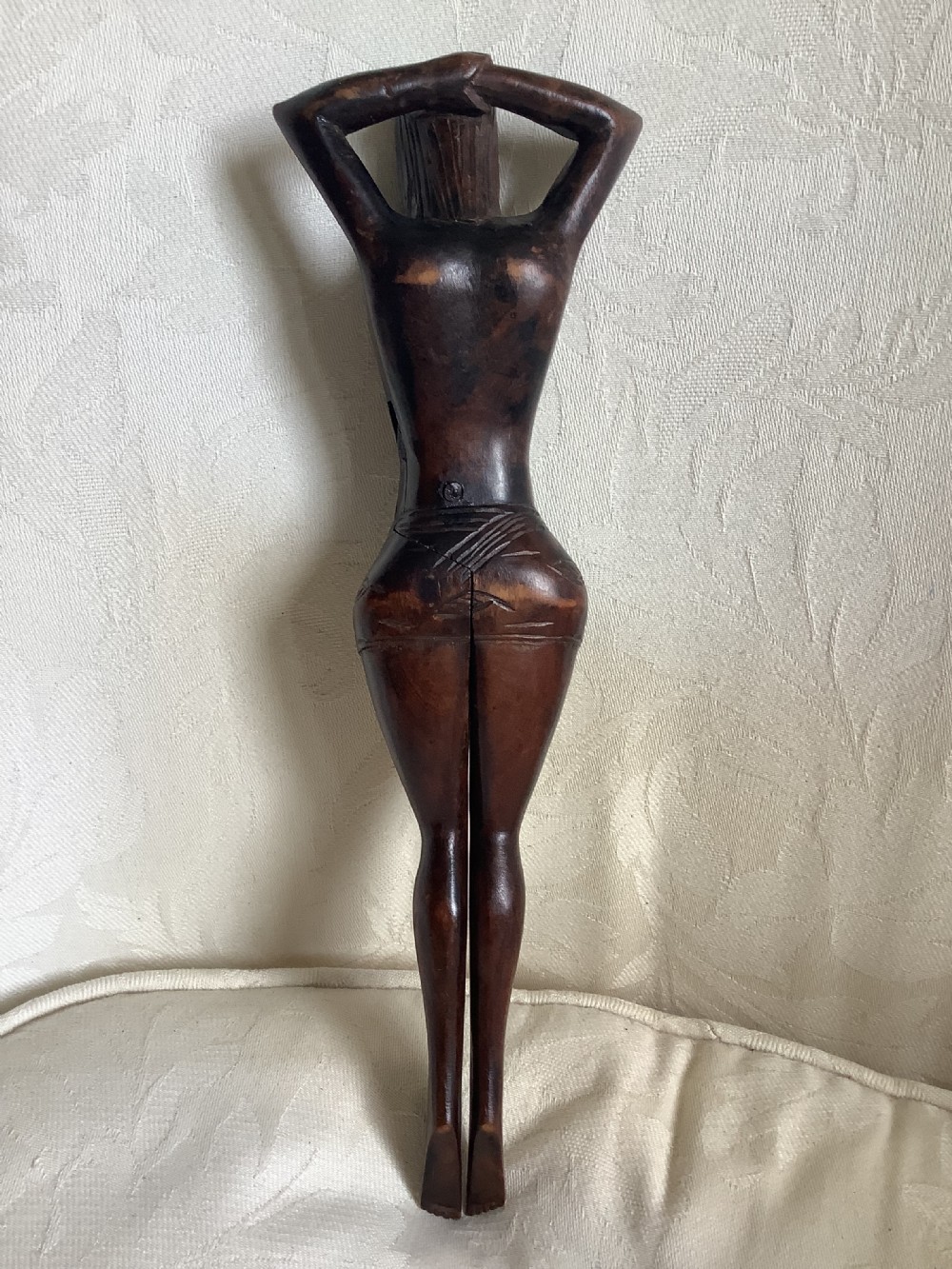 A hand-carved dark wood nutcracker sculpted in the form of a standing woman with her arms raised behind her head. View VI