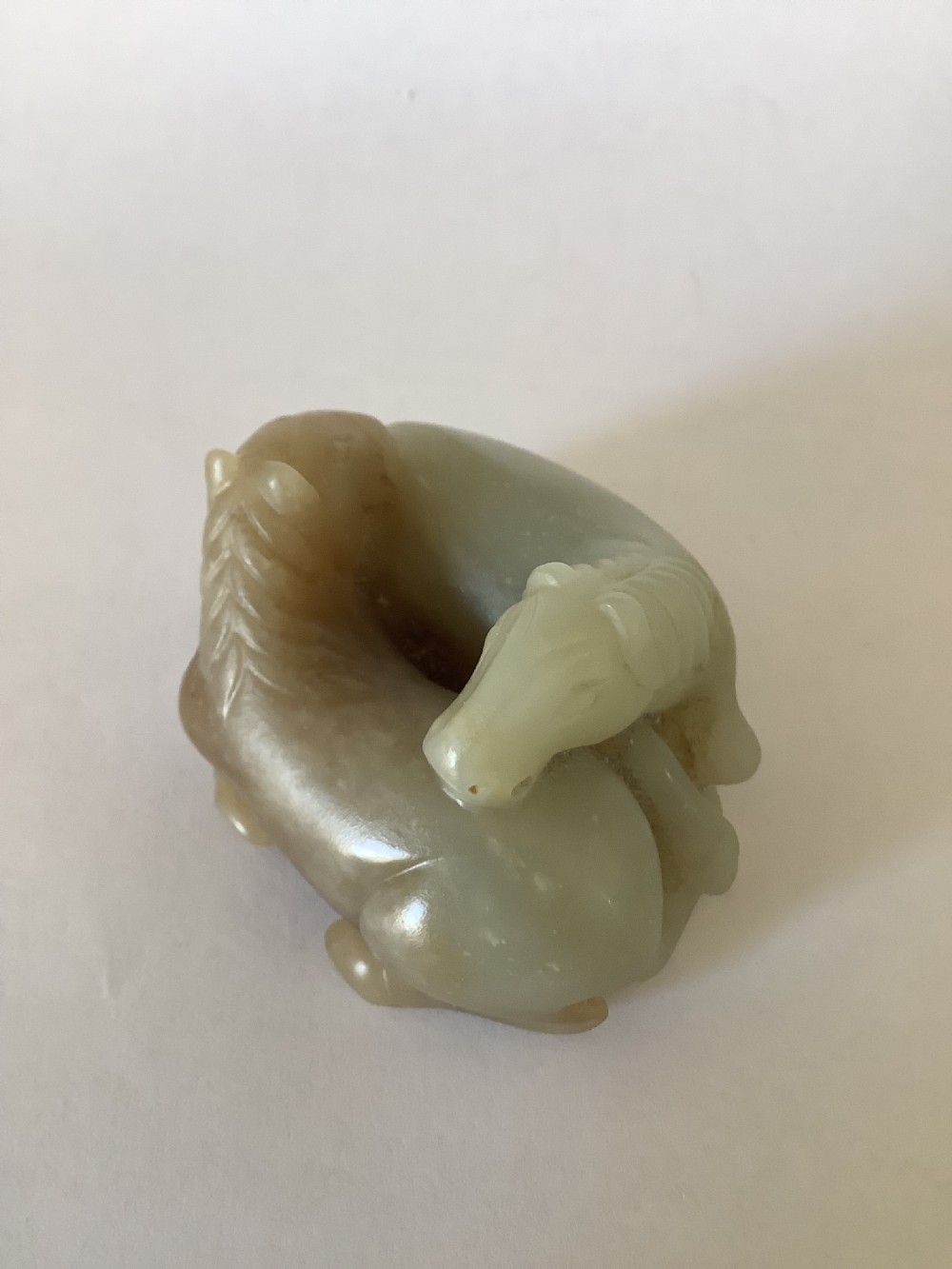 A small 19th-century Chinese hand-carved jade sculpture depicting two intertwined recumbent horses in pale celadon green and grey hardstone. View II