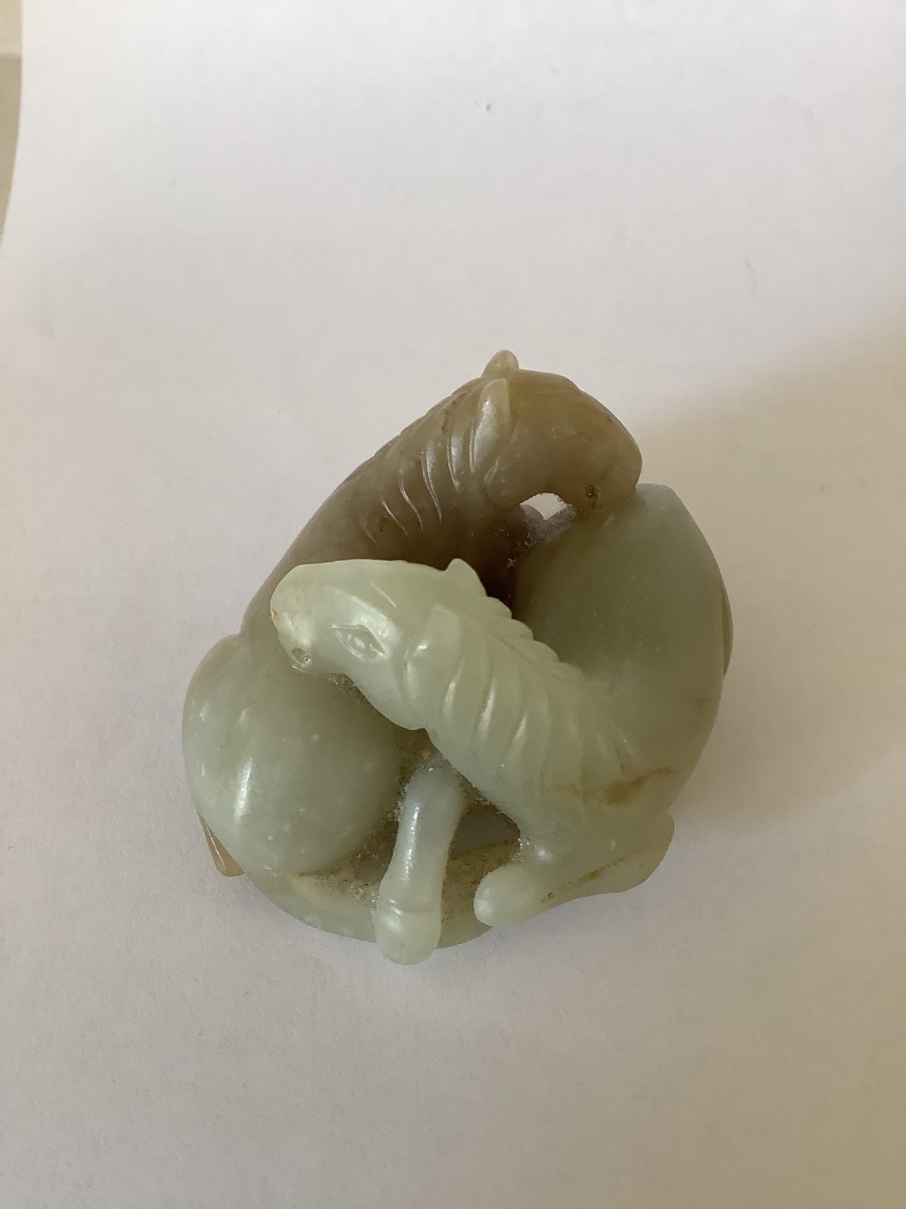 A small 19th-century Chinese hand-carved jade sculpture depicting two intertwined recumbent horses in pale celadon green and grey hardstone. View III