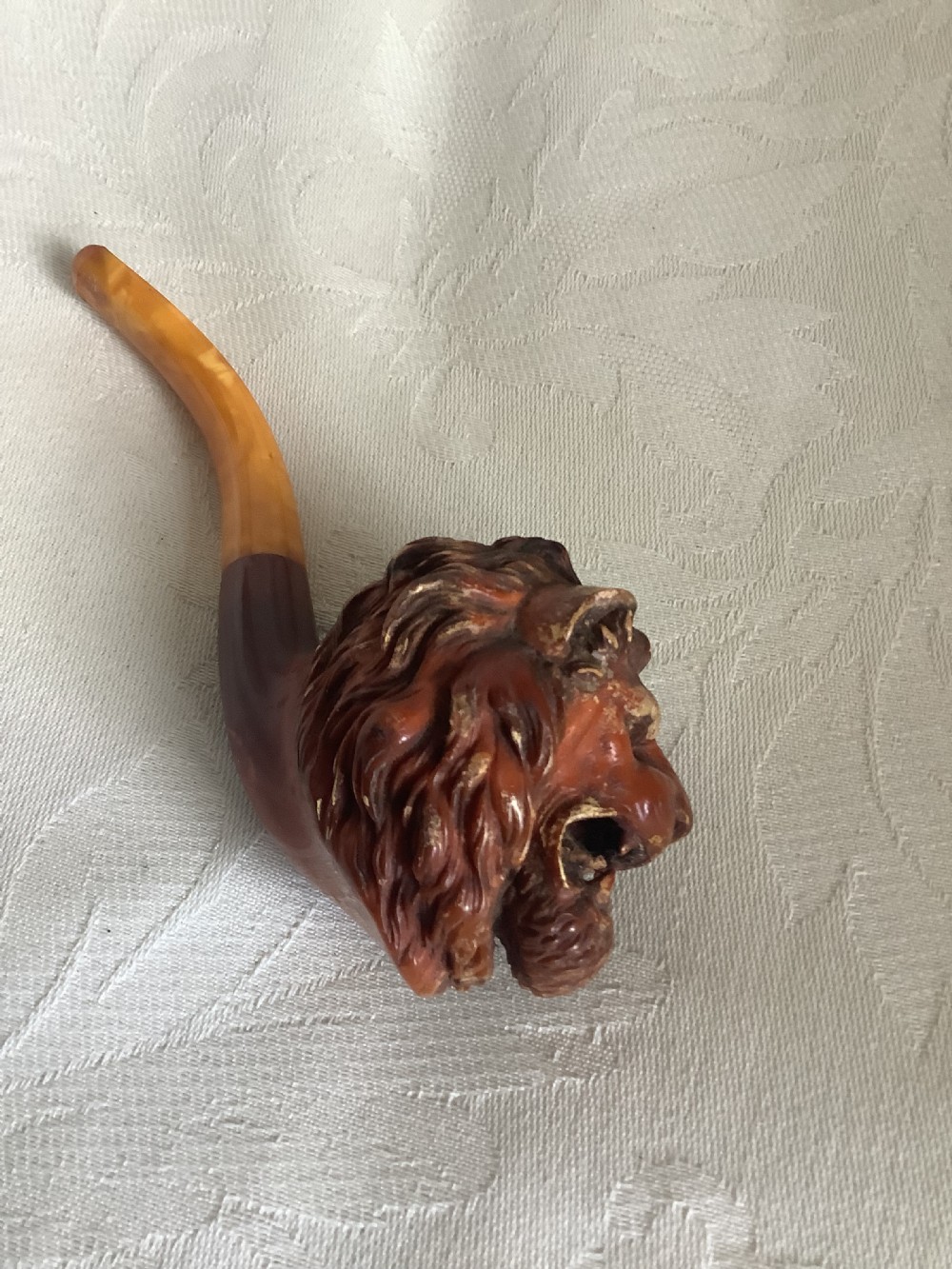 A hand-carved meerschaum smoking pipe featuring a detailed lion head bowl with an open mouth and a translucent amber-coloured curved stem. View II