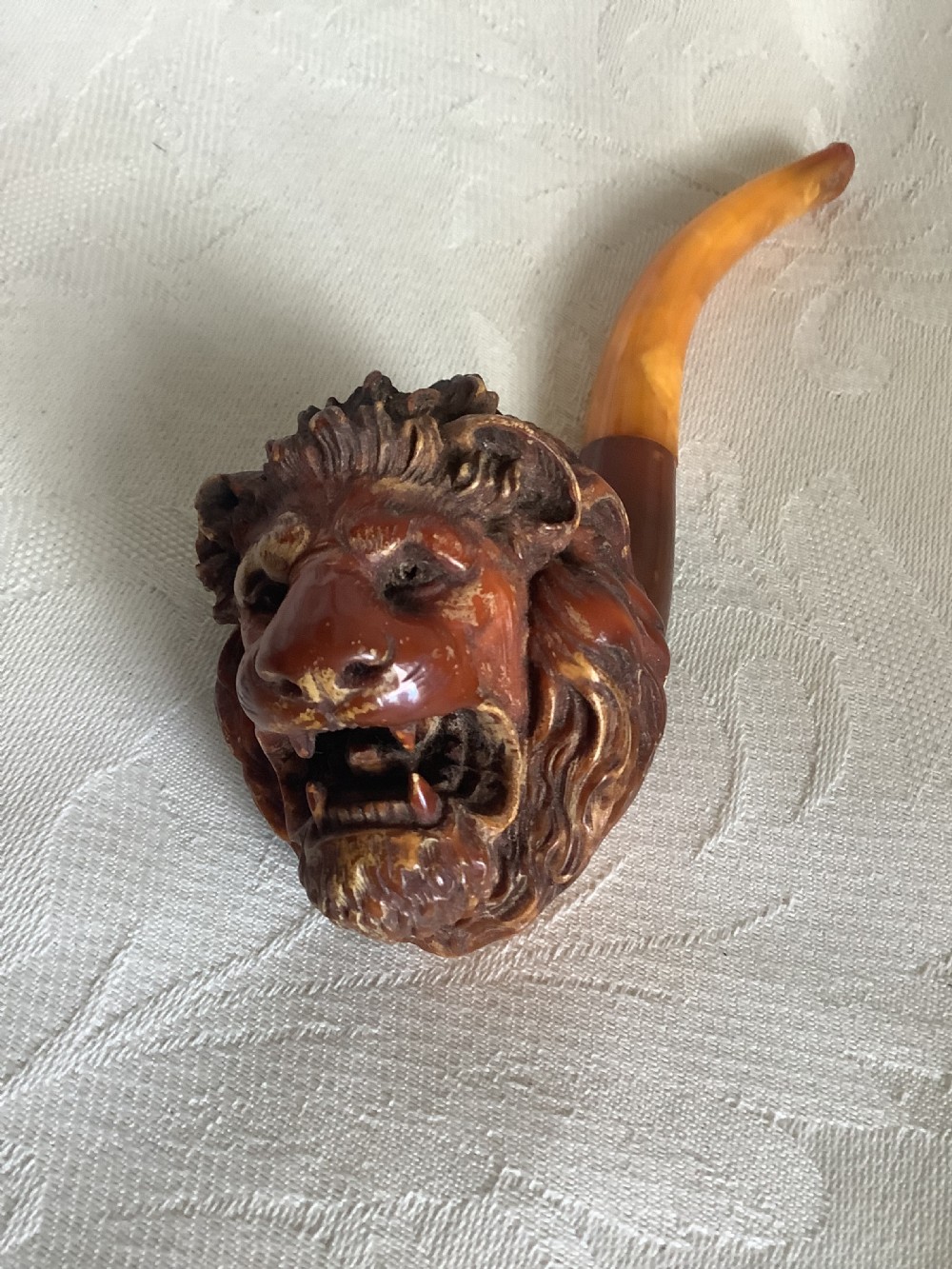 A hand-carved meerschaum smoking pipe featuring a detailed lion head bowl with an open mouth and a translucent amber-coloured curved stem. View IV