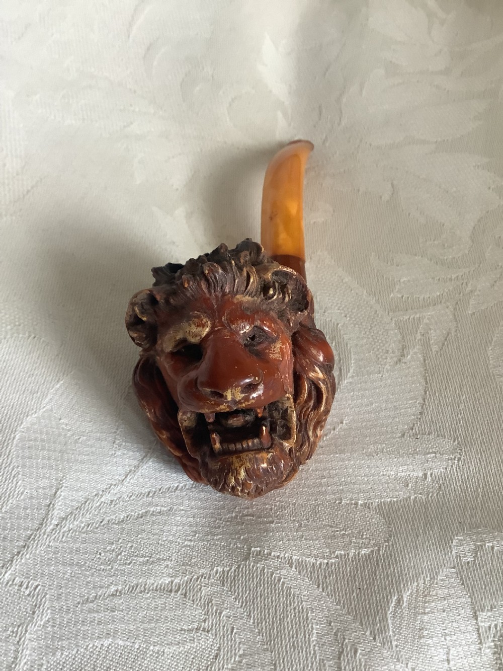 A hand-carved meerschaum smoking pipe featuring a detailed lion head bowl with an open mouth and a translucent amber-coloured curved stem. View V