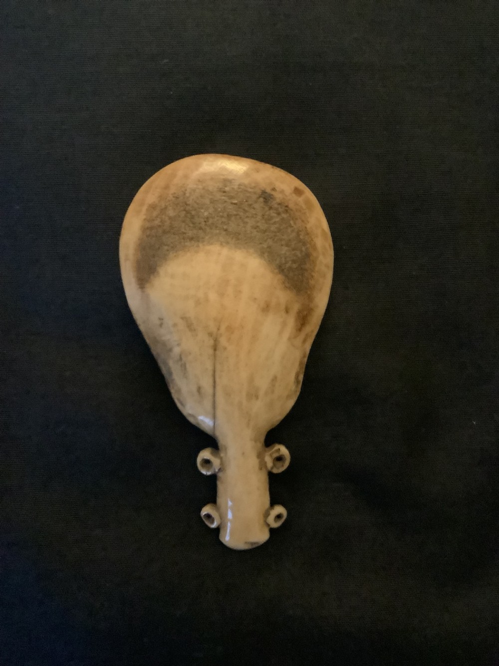 A hand-carved bone or antler spoon featuring an etched drawing of a caribou on the shallow cream-coloured bowl and a textured handle with four side loops. View II