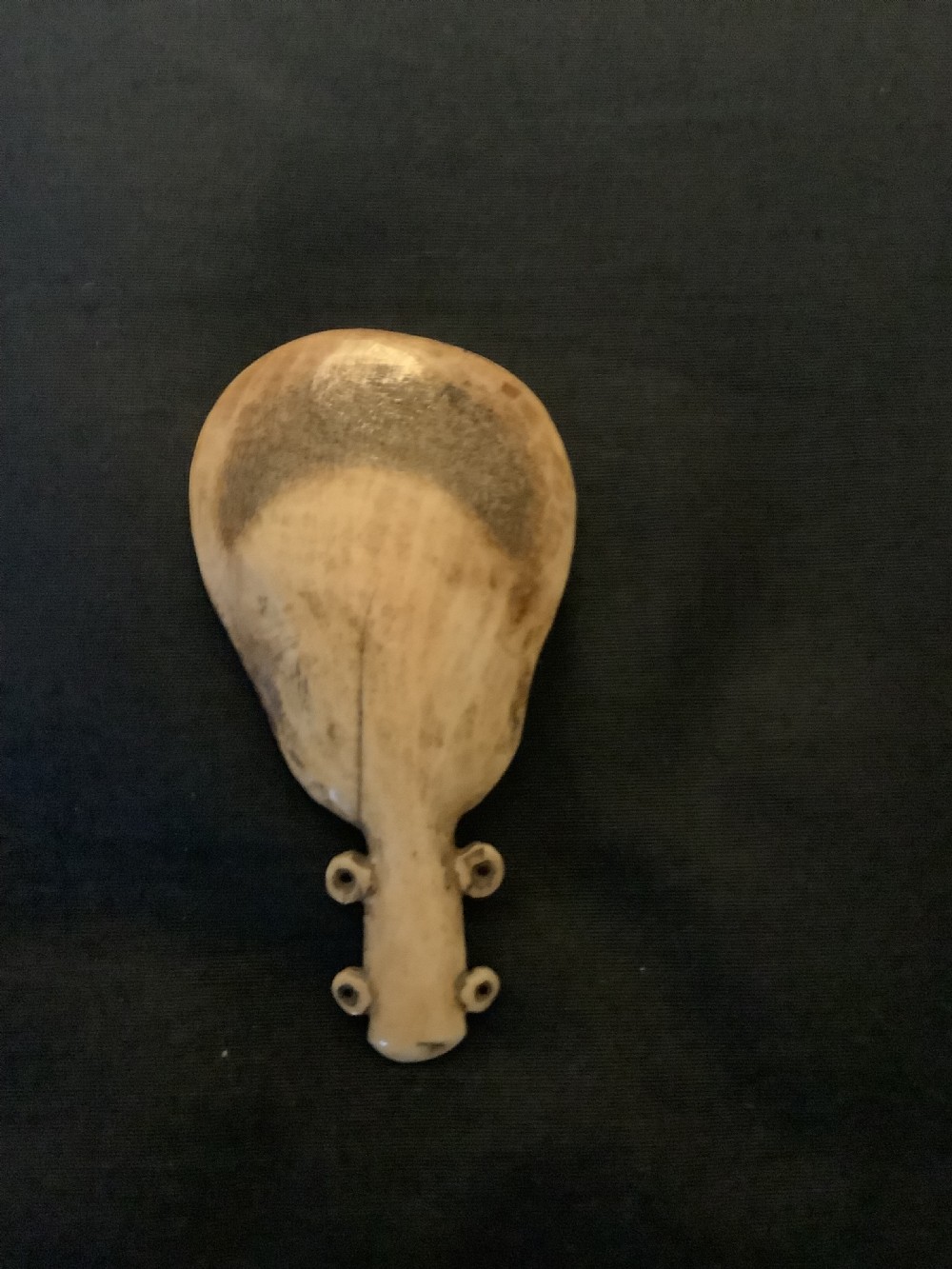 A hand-carved bone or antler spoon featuring an etched drawing of a caribou on the shallow cream-coloured bowl and a textured handle with four side loops. View VII