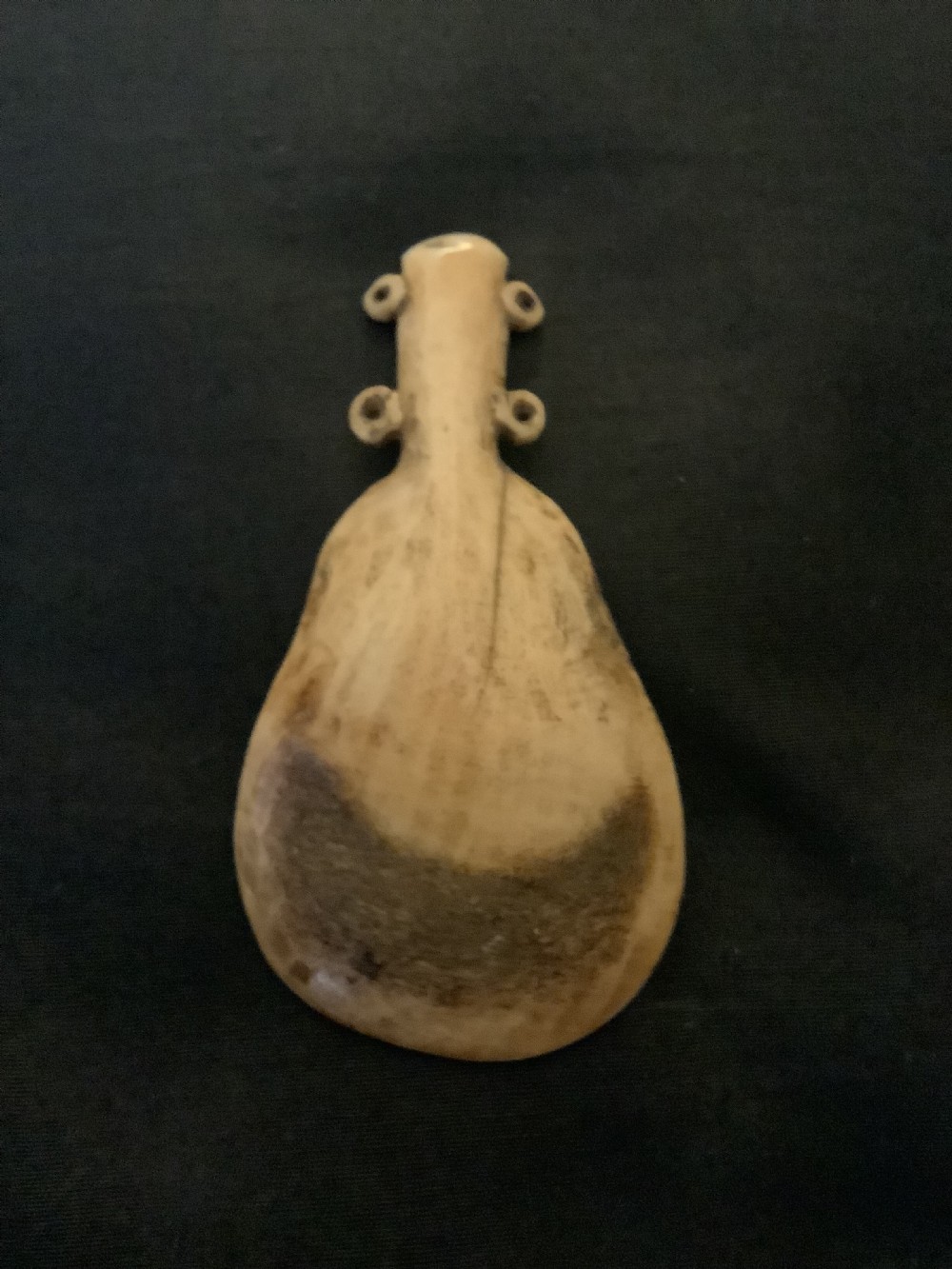 A hand-carved bone or antler spoon featuring an etched drawing of a caribou on the shallow cream-coloured bowl and a textured handle with four side loops. View IX