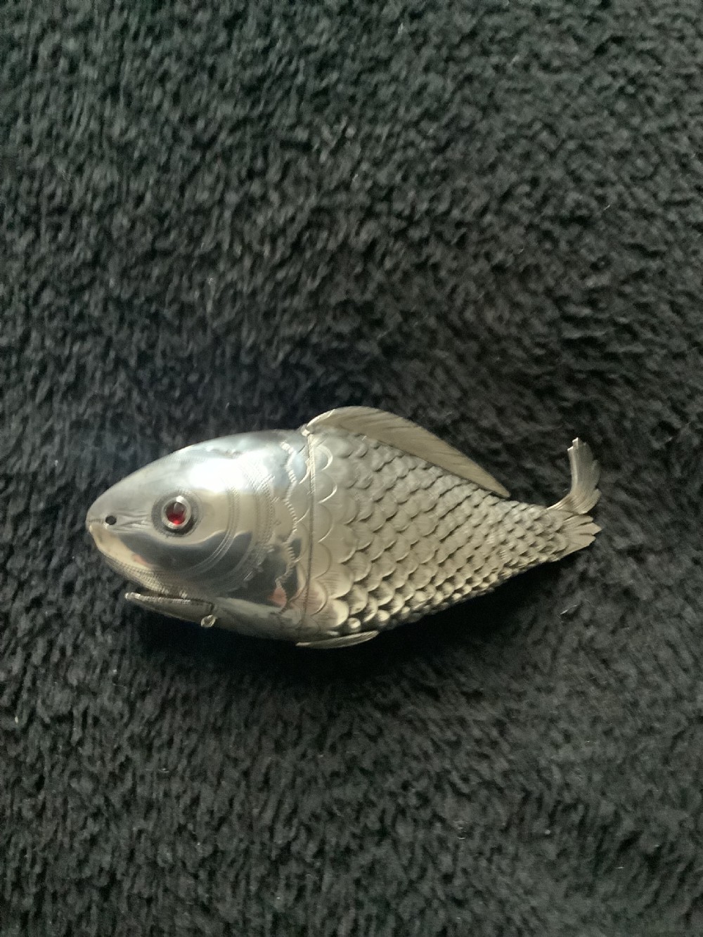 A silver fish-shaped box featuring engraved scales, an articulated body, a hinged head opening, and a red glass eye. View VIII