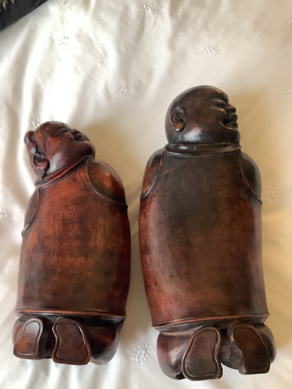 A pair of carved brown bamboo headrests depicted as rounded smiling figures with smooth polished surfaces. View II
