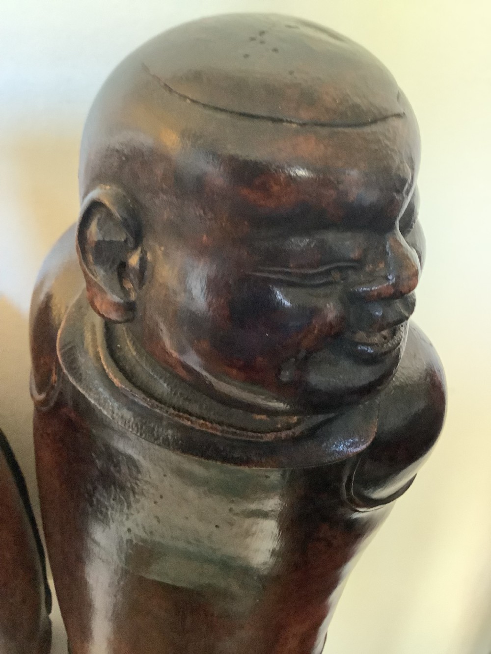 A pair of carved brown bamboo headrests depicted as rounded smiling figures with smooth polished surfaces. View VI