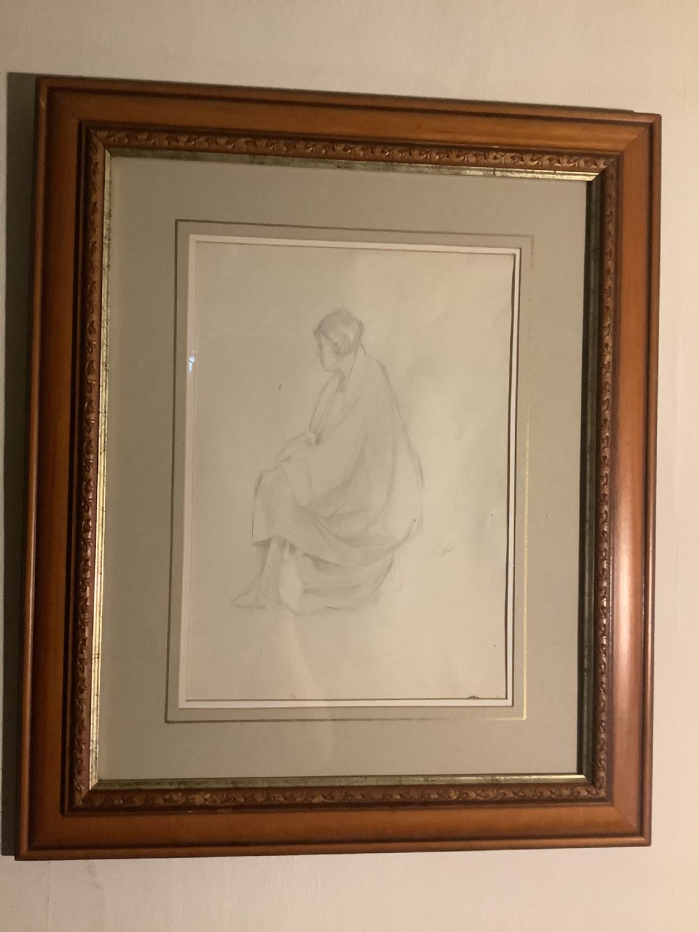 A framed monochrome pencil sketch depicting a seated draped female figure, presented in a neutral double mount within a moulded wooden frame.
