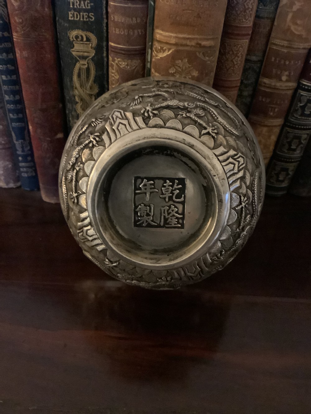 A circular silver-coloured metal bowl decorated with high-relief Chinese dragons chasing a flaming pearl above a key fret foot rim. View II