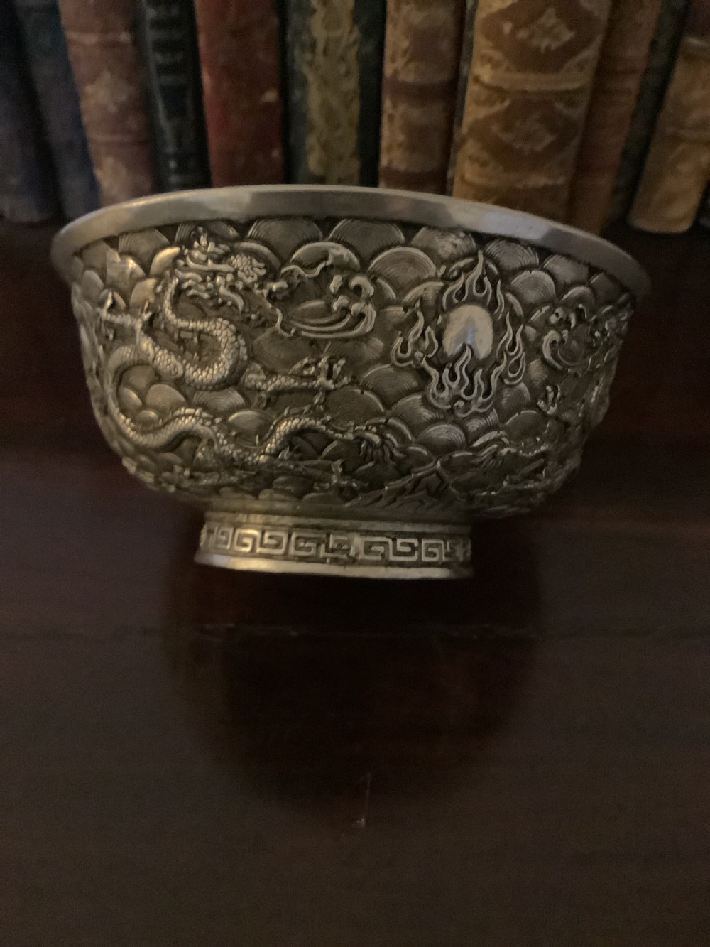 A circular silver-coloured metal bowl decorated with high-relief Chinese dragons chasing a flaming pearl above a key fret foot rim. View III