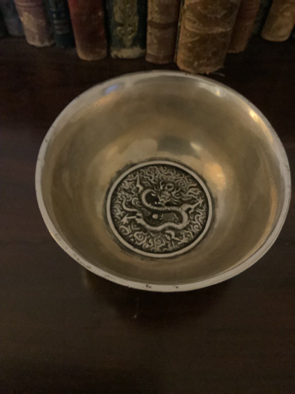 A circular silver-coloured metal bowl decorated with high-relief Chinese dragons chasing a flaming pearl above a key fret foot rim. View IV