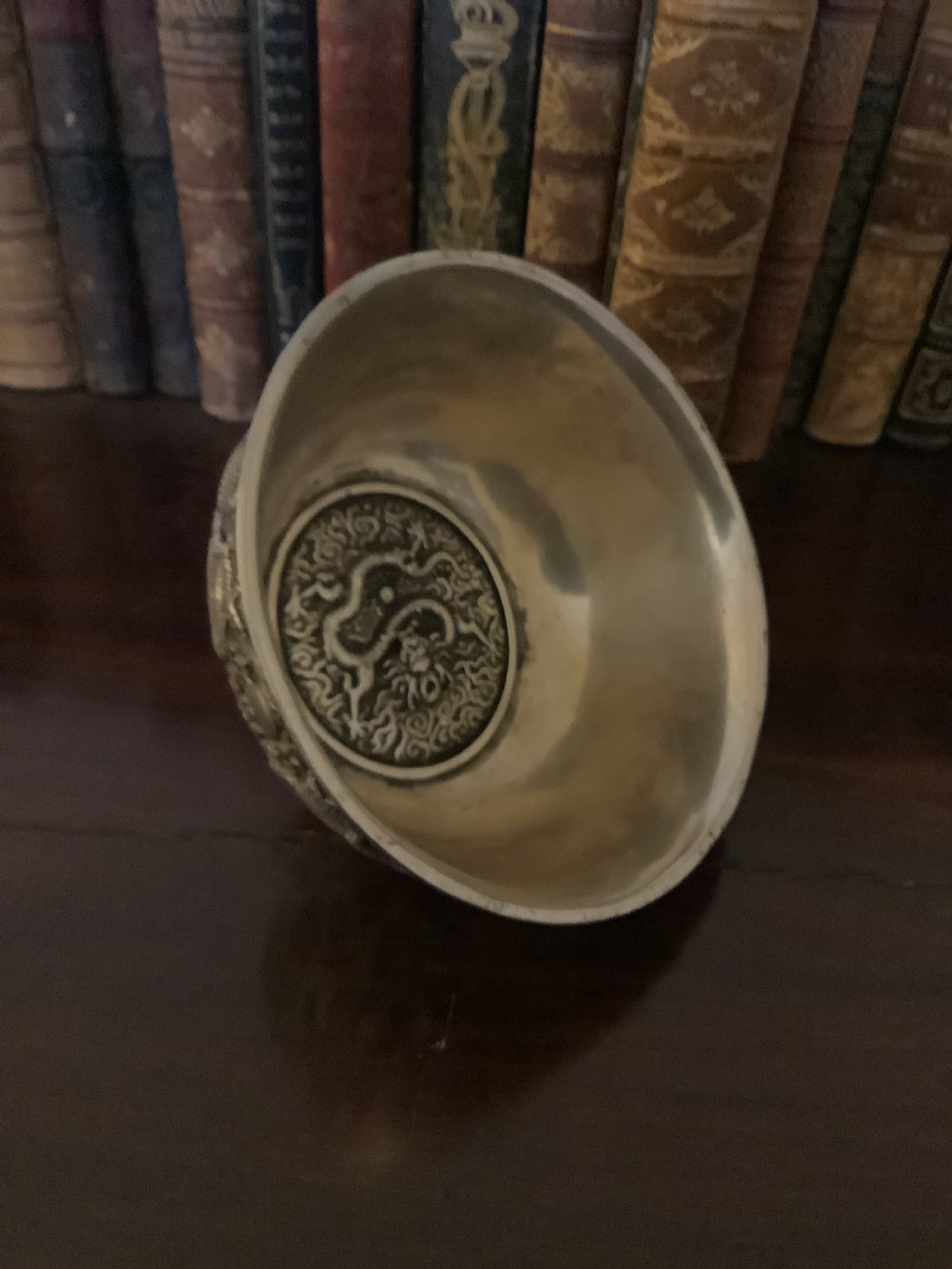 A circular silver-coloured metal bowl decorated with high-relief Chinese dragons chasing a flaming pearl above a key fret foot rim. View V