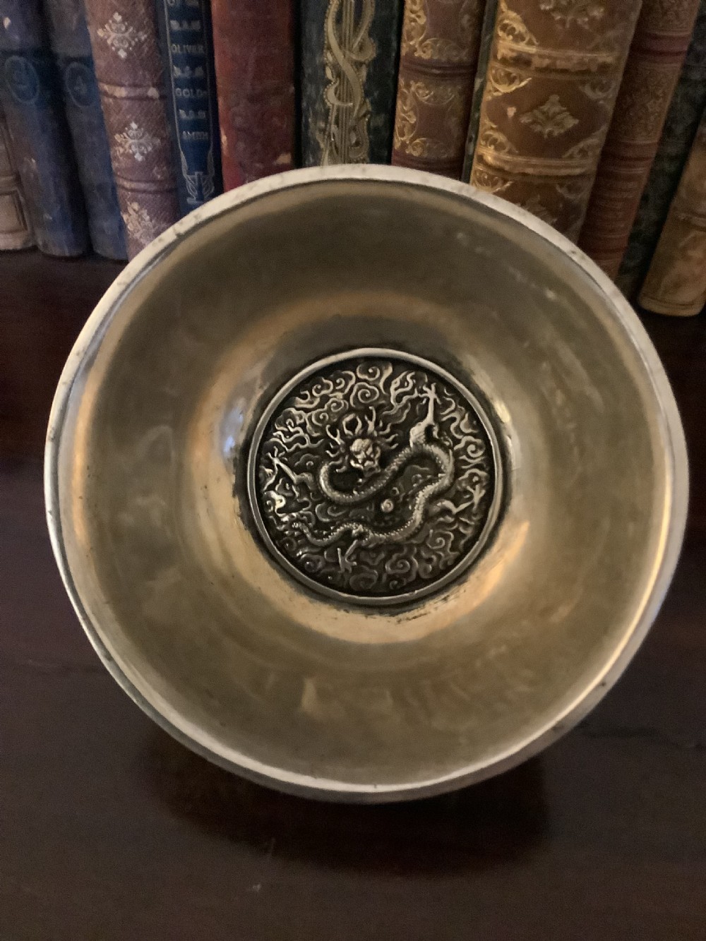 A circular silver-coloured metal bowl decorated with high-relief Chinese dragons chasing a flaming pearl above a key fret foot rim. View VI