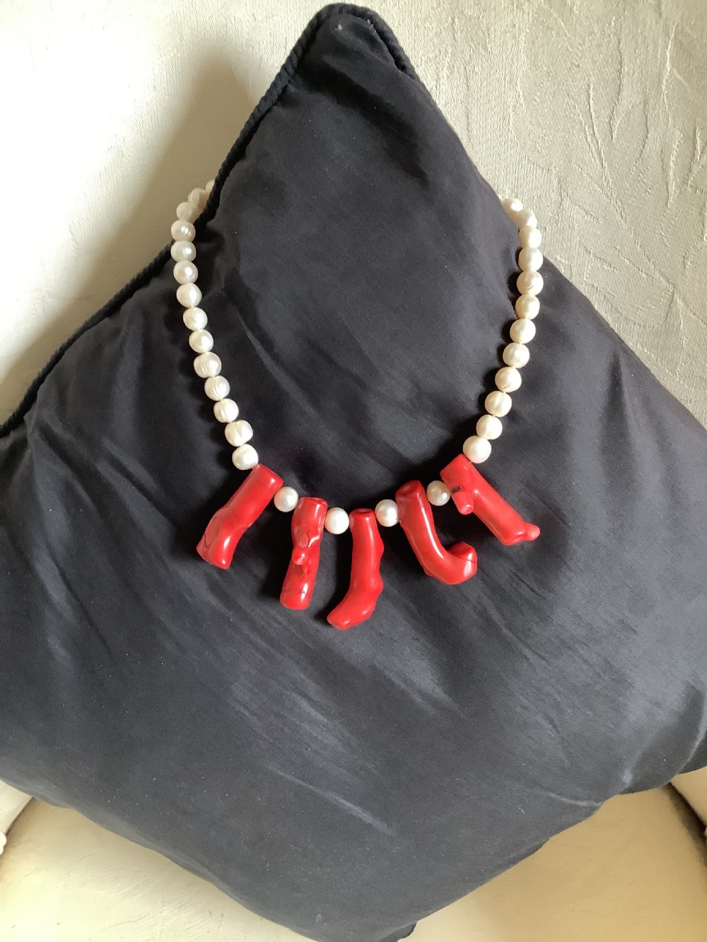 A necklace featuring a strand of rounded white pearls accented by five suspended polished red coral branches at the front centre.