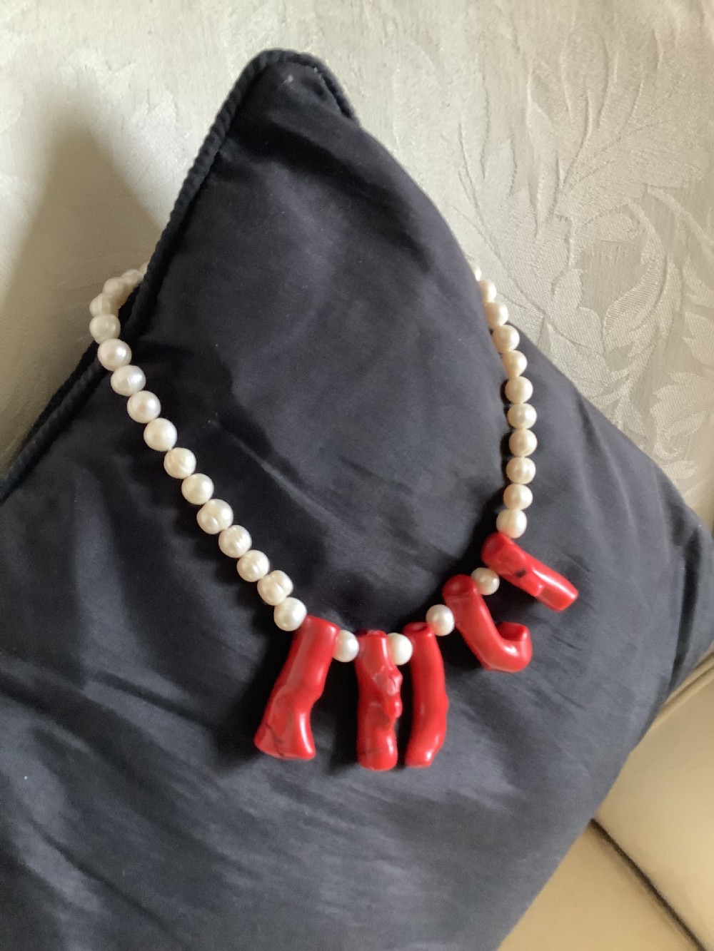 A necklace featuring a strand of rounded white pearls accented by five suspended polished red coral branches at the front centre. View II