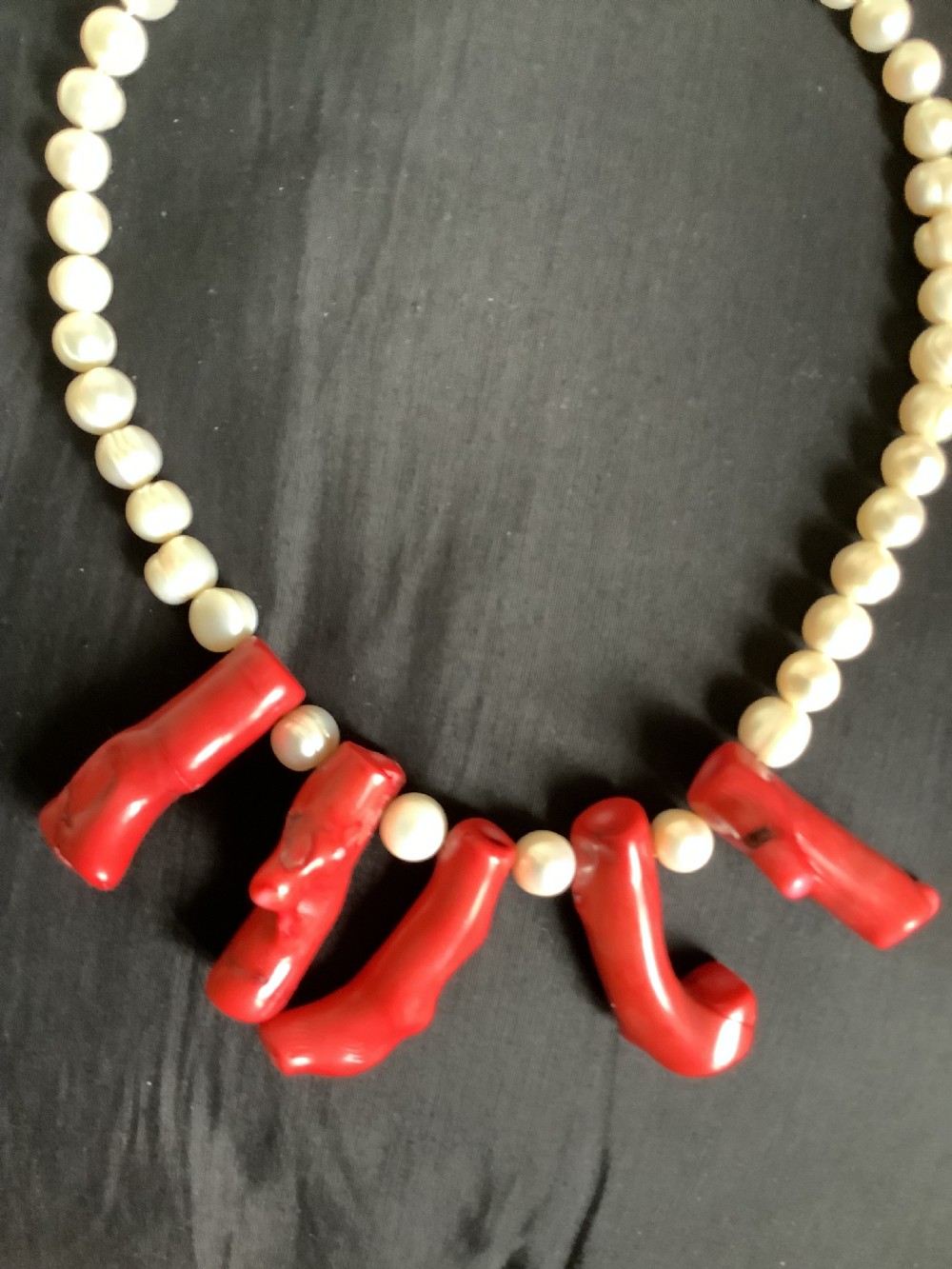 A necklace featuring a strand of rounded white pearls accented by five suspended polished red coral branches at the front centre. View IV