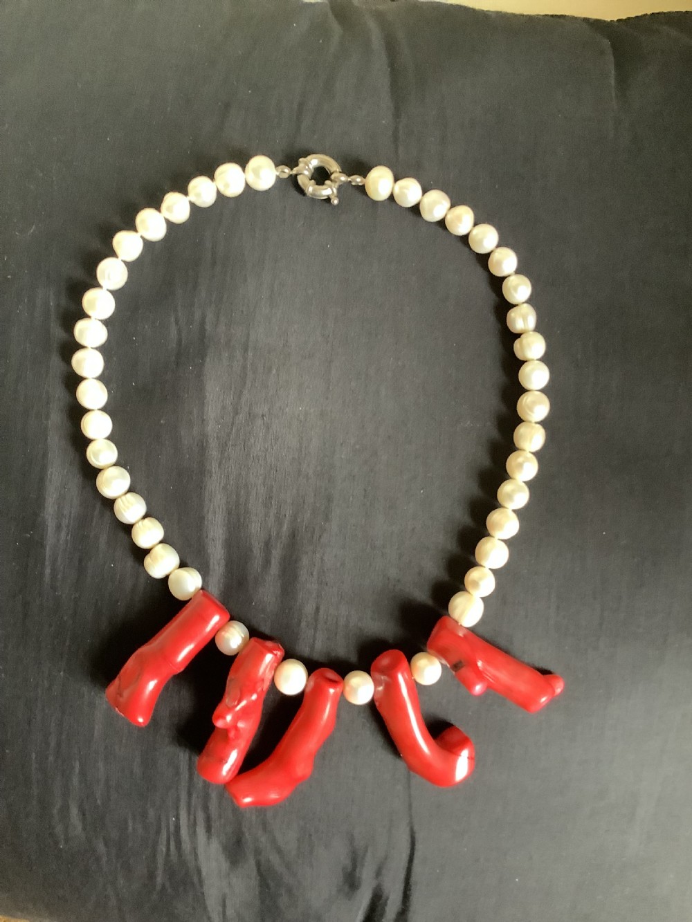 A necklace featuring a strand of rounded white pearls accented by five suspended polished red coral branches at the front centre. View V