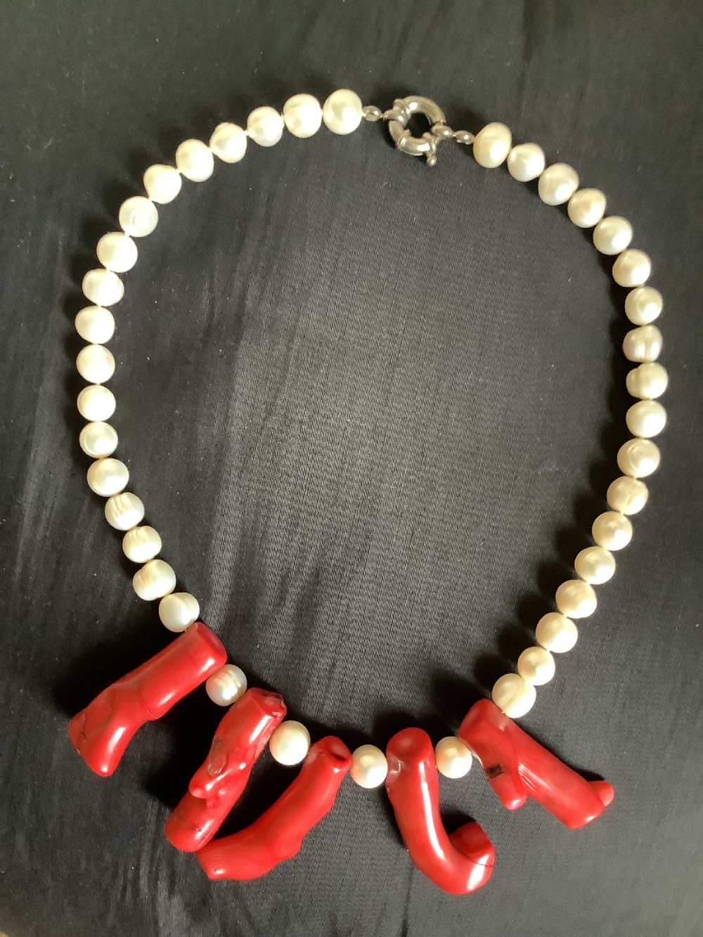 A necklace featuring a strand of rounded white pearls accented by five suspended polished red coral branches at the front centre. View VI
