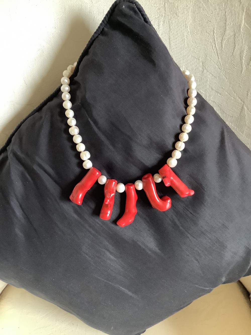 A necklace featuring a strand of rounded white pearls accented by five suspended polished red coral branches at the front centre. View VII