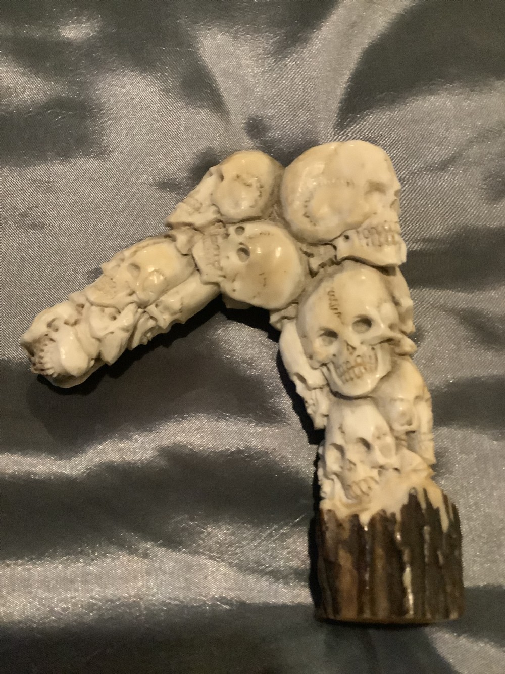 A carved stag horn walking stick handle shaped with a dense cluster of sculpted human skulls atop a natural textured antler base.