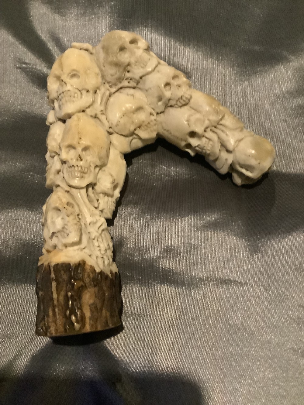 A carved stag horn walking stick handle shaped with a dense cluster of sculpted human skulls atop a natural textured antler base. View II