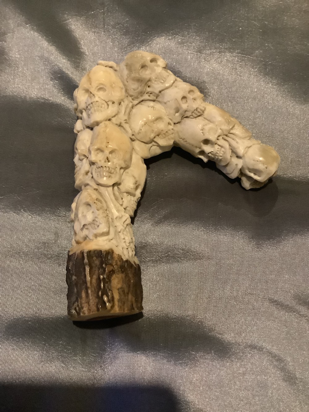A carved stag horn walking stick handle shaped with a dense cluster of sculpted human skulls atop a natural textured antler base. View III