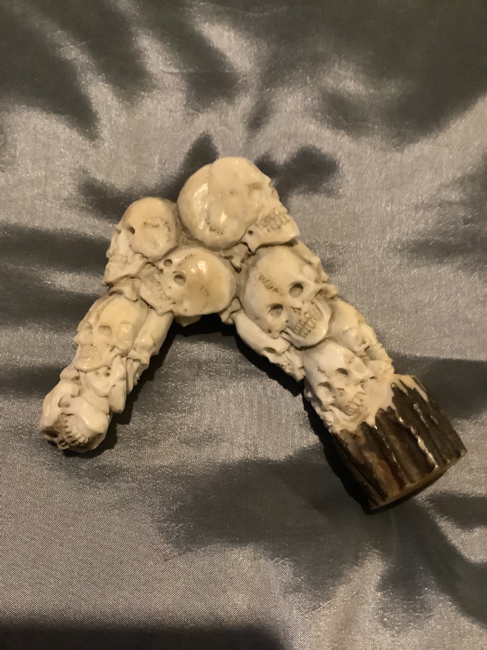 A carved stag horn walking stick handle shaped with a dense cluster of sculpted human skulls atop a natural textured antler base. View IV