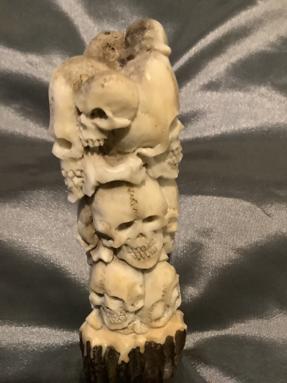 A carved stag horn walking stick handle shaped with a dense cluster of sculpted human skulls atop a natural textured antler base. View V