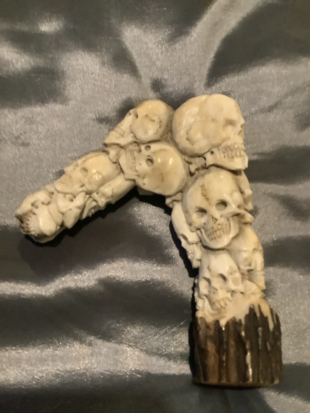 A carved stag horn walking stick handle shaped with a dense cluster of sculpted human skulls atop a natural textured antler base. View VI