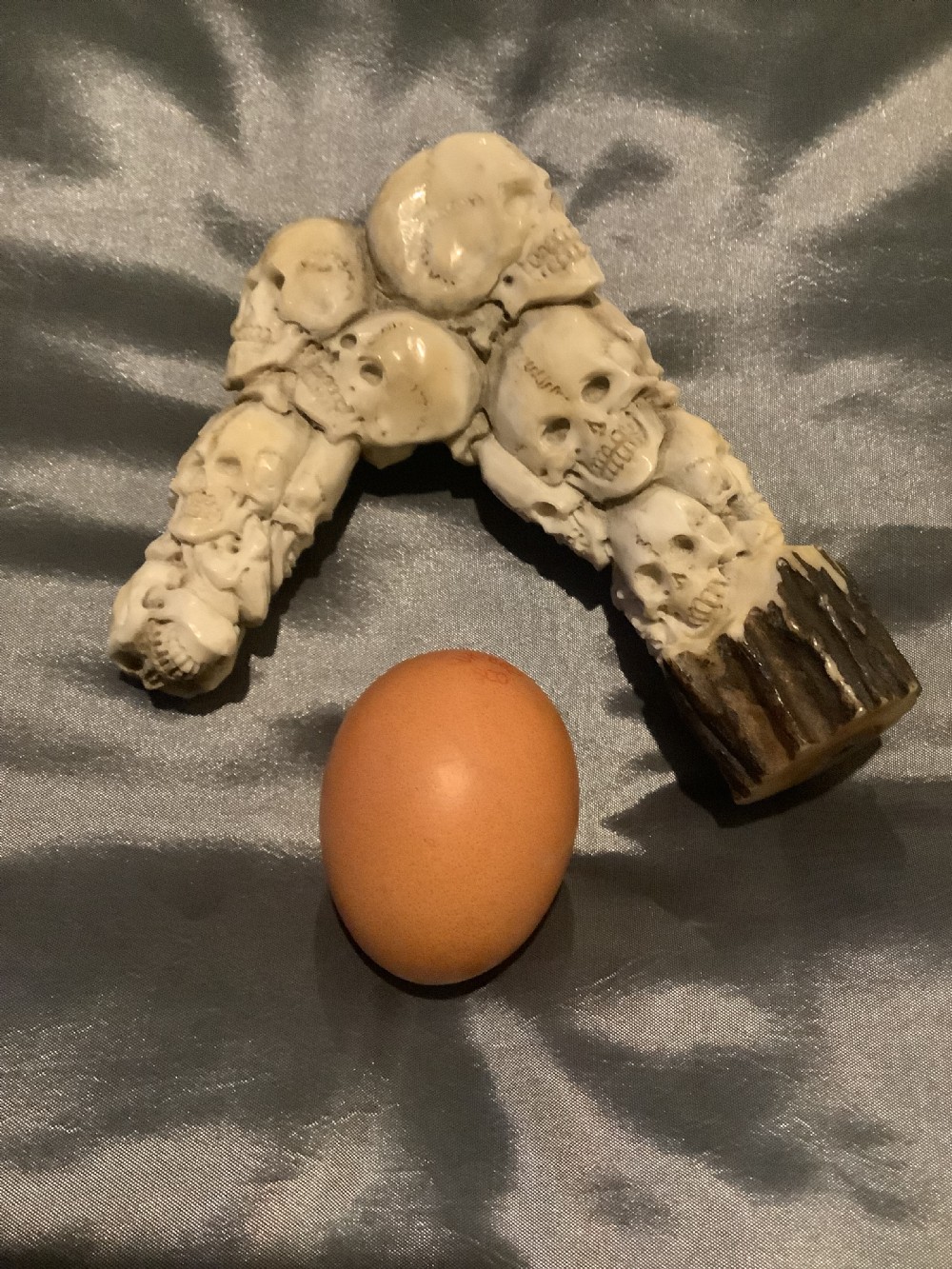 A carved stag horn walking stick handle shaped with a dense cluster of sculpted human skulls atop a natural textured antler base. View VII