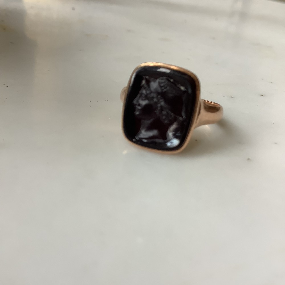 A gold ring set with a cushion-shaped dark gemstone featuring an intaglio-carved classical profile portrait.
