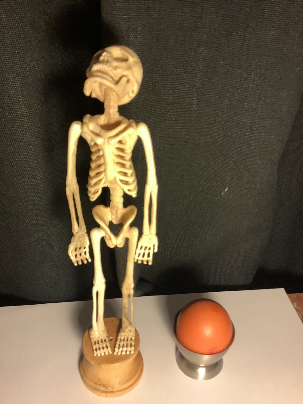 A carved cream-coloured miniature human skeleton standing upright on a round turned wooden plinth against a light backdrop. View VII