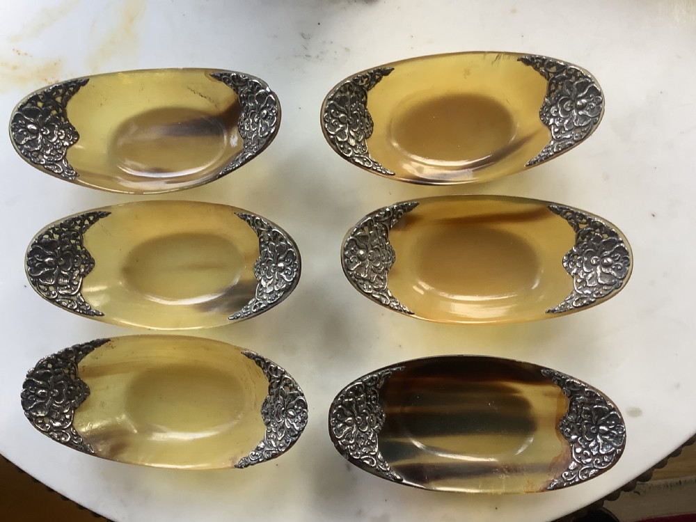A set of seven oval amber-toned horn bowls featuring carved floral silver mounts at each end. View III