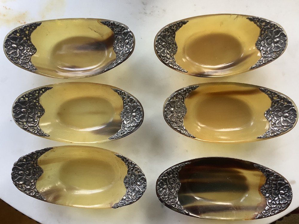 A set of seven oval amber-toned horn bowls featuring carved floral silver mounts at each end. View IV
