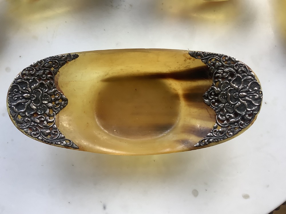 A set of seven oval amber-toned horn bowls featuring carved floral silver mounts at each end. View VI