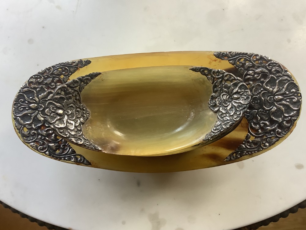 A set of seven oval amber-toned horn bowls featuring carved floral silver mounts at each end. View VII
