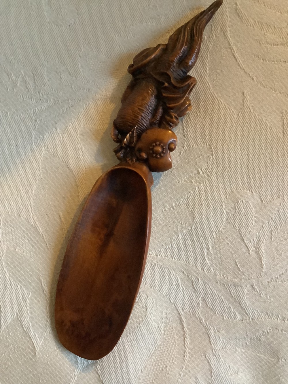 A hand-carved warm brown hardwood tea scoop featuring detailed figurative relief work along the upper handle. View VII