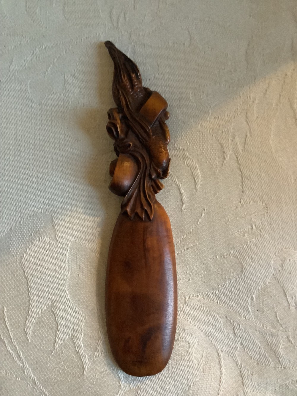 A hand-carved warm brown hardwood tea scoop featuring detailed figurative relief work along the upper handle. View III