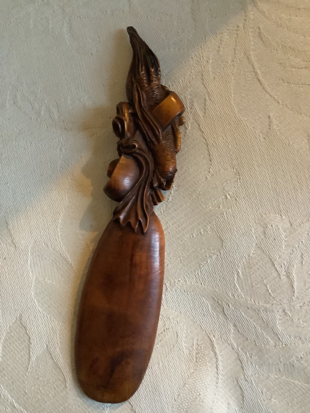 A hand-carved warm brown hardwood tea scoop featuring detailed figurative relief work along the upper handle. View IV