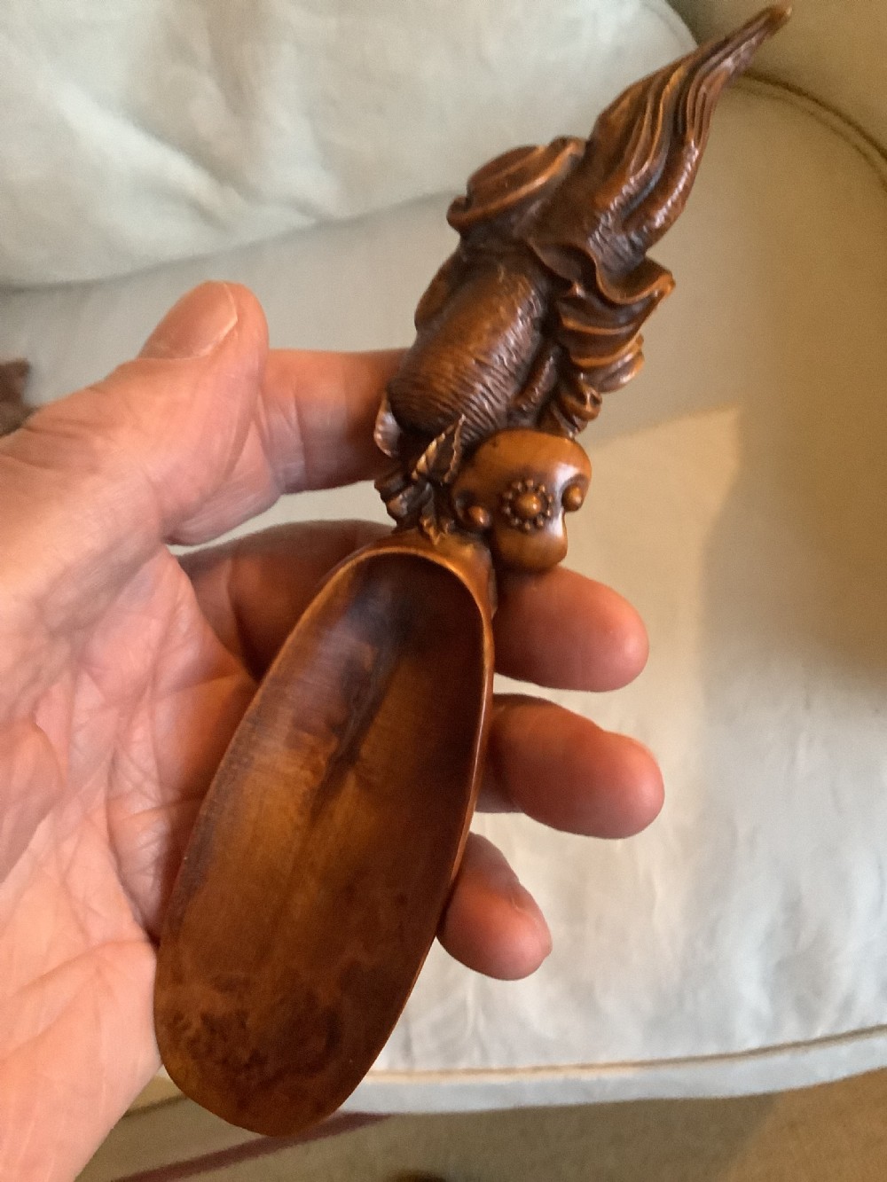 A hand-carved warm brown hardwood tea scoop featuring detailed figurative relief work along the upper handle. View V