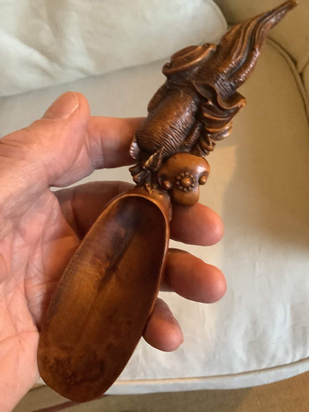A hand-carved warm brown hardwood tea scoop featuring detailed figurative relief work along the upper handle.