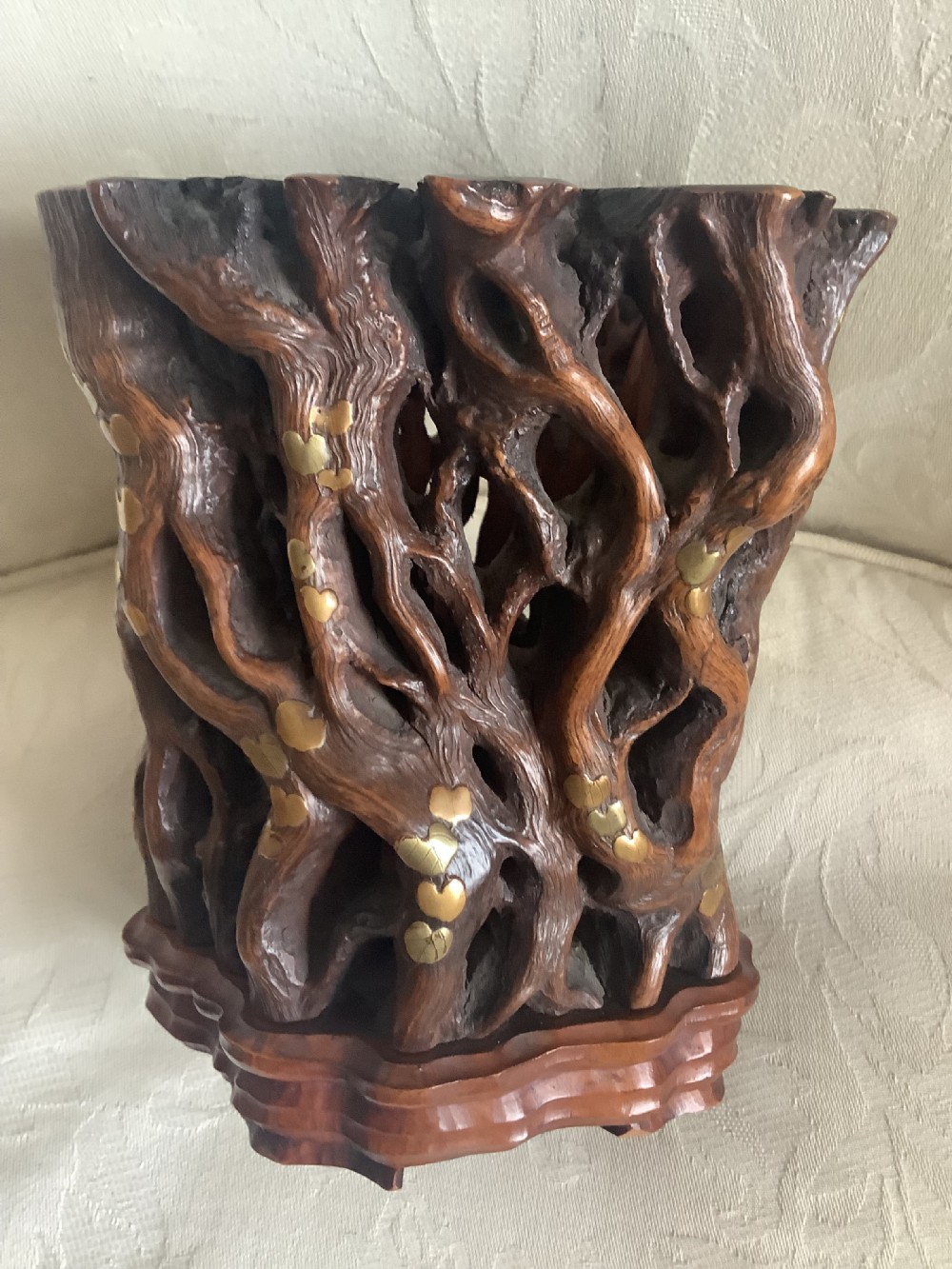 A dark brown carved hardwood brush pot featuring natural gnarled openwork root design with brass leaf inlays, resting on a carved base. View III