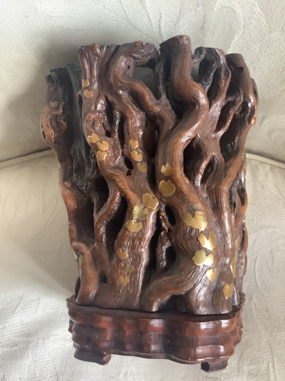 A dark brown carved hardwood brush pot featuring natural gnarled openwork root design with brass leaf inlays, resting on a carved base. View V