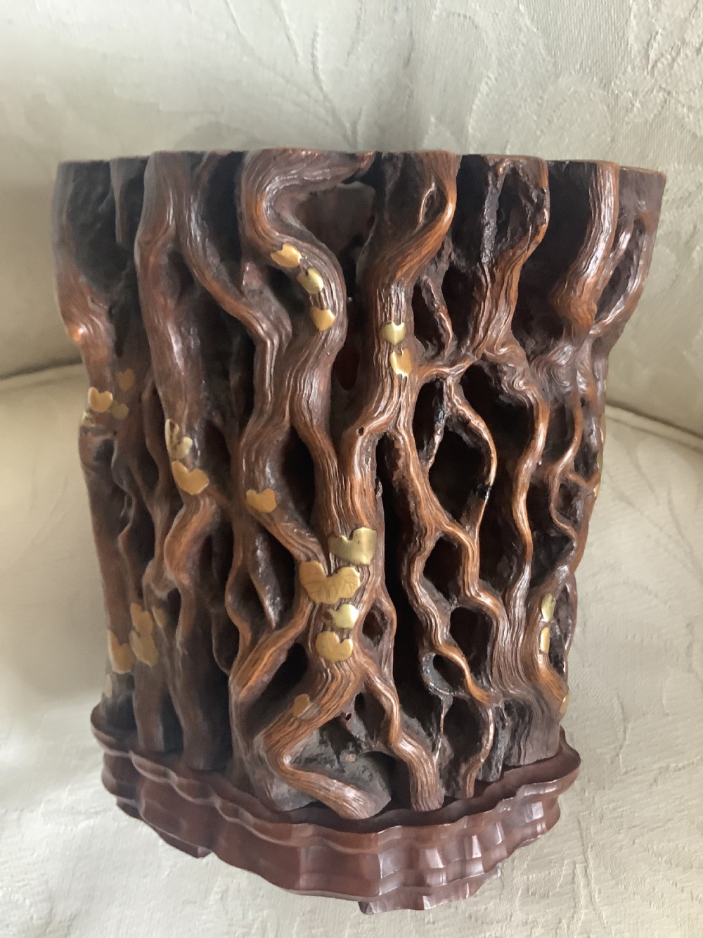 A dark brown carved hardwood brush pot featuring natural gnarled openwork root design with brass leaf inlays, resting on a carved base. View VI