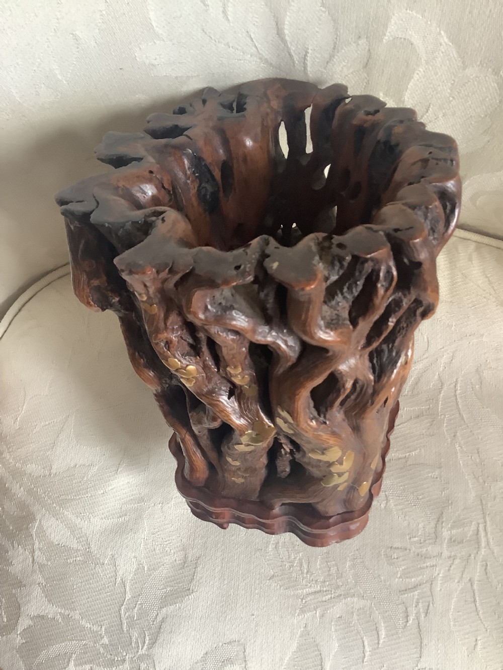 A dark brown carved hardwood brush pot featuring natural gnarled openwork root design with brass leaf inlays, resting on a carved base. View VIII