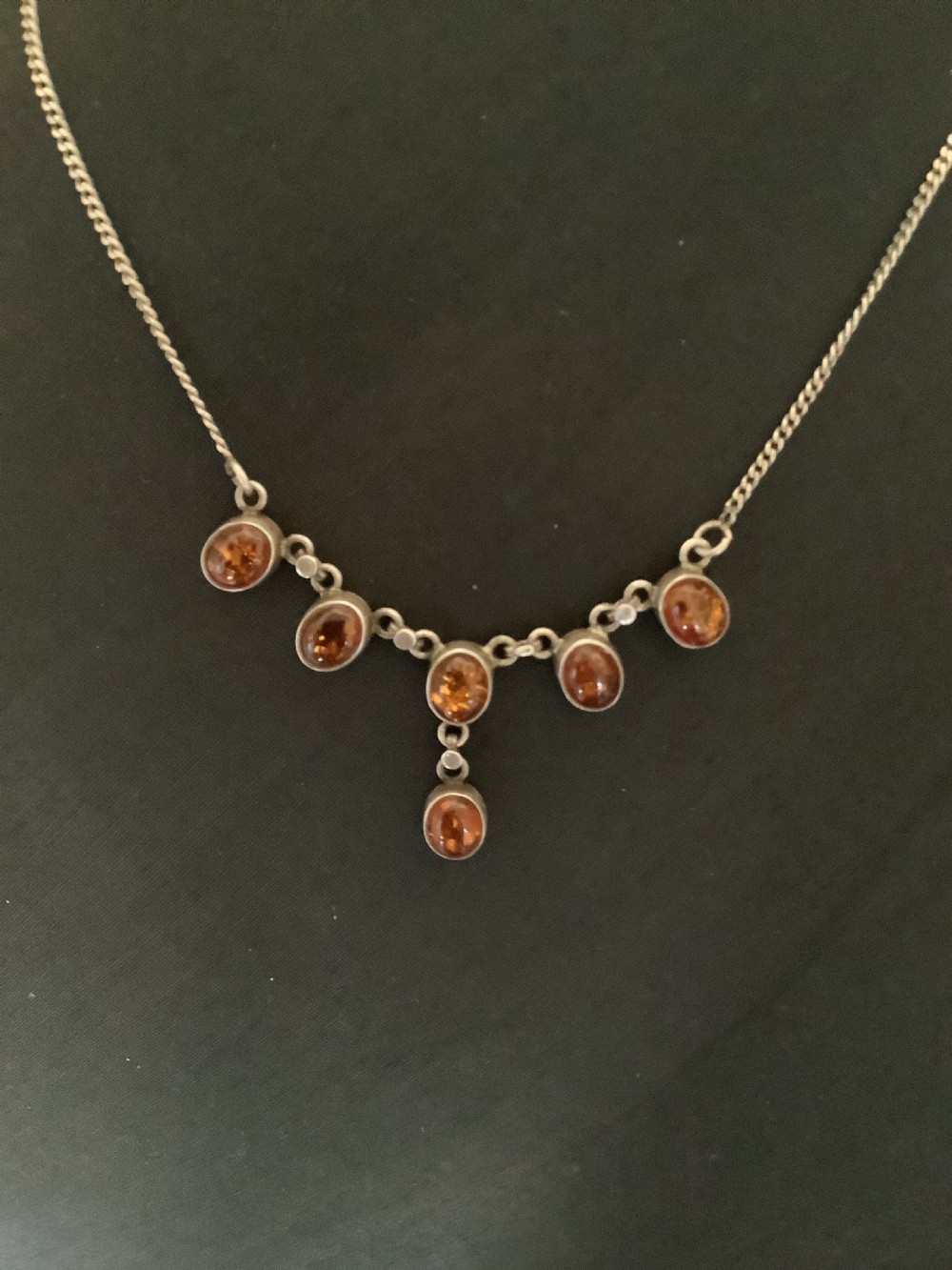 A fine silver chain necklace featuring six bezel-set oval cognac amber cabochons arranged in a central drop configuration. View V