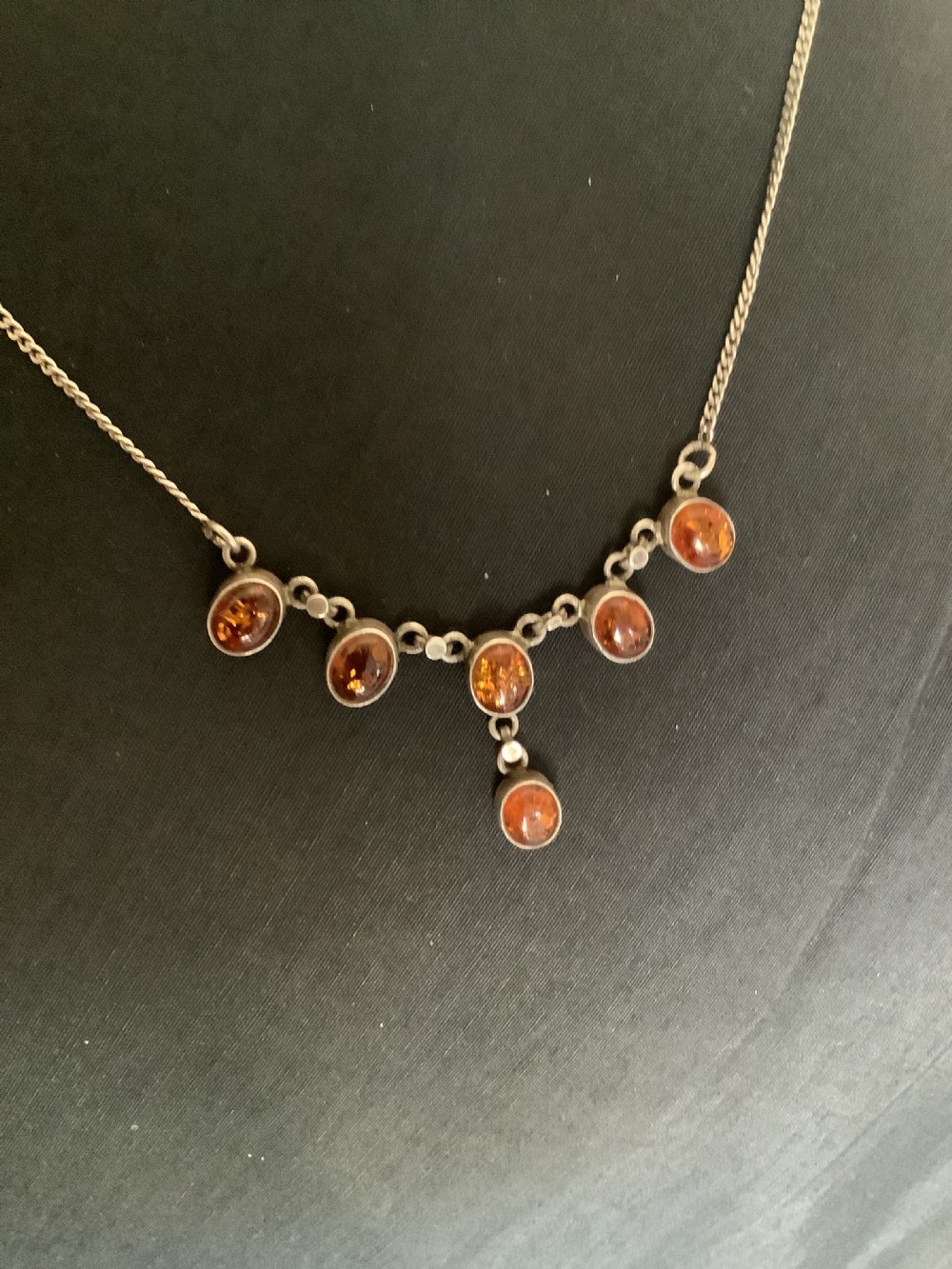 A fine silver chain necklace featuring six bezel-set oval cognac amber cabochons arranged in a central drop configuration. View VI