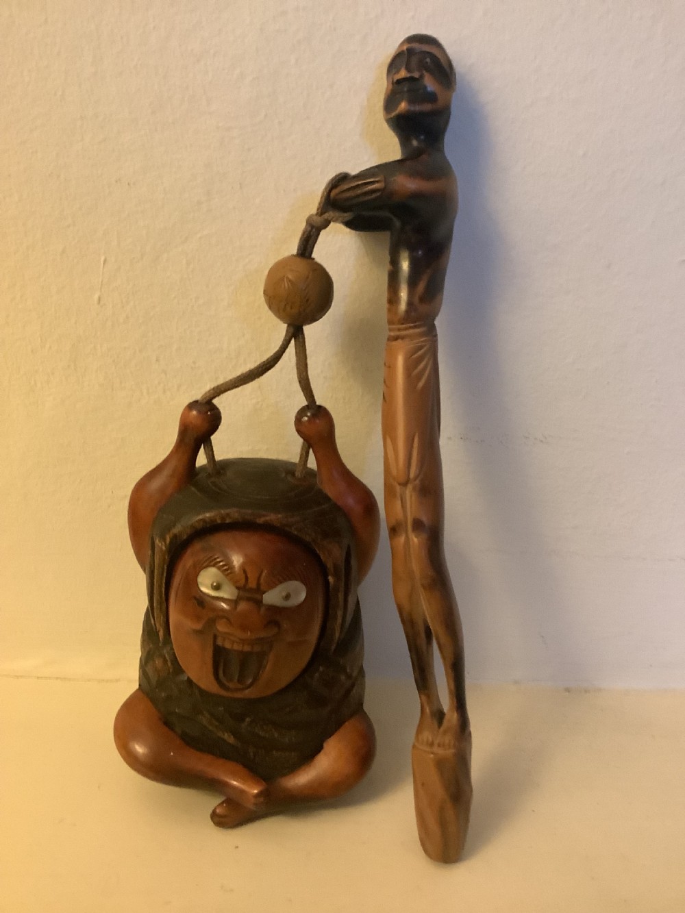 A carved wooden Japanese tobacco container featuring a wide-eyed Daruma figure connected by a cord and bead to an elongated carved wooden pipe holder.